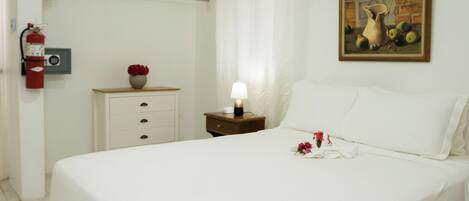 A neatly made bed with a white bedspread, a nightstand with a lamp, and a painting on the wall.