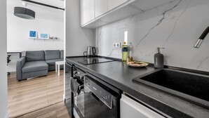 A modern kitchen with a black countertop, stainless steel appliances, and a marble backsplash. - Mokotów Studio- 14th Floor, Balcony - by Rentujemy (Warszawa)
