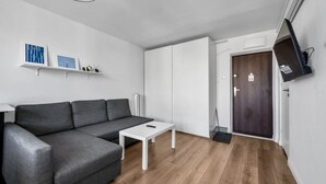 A modern living room with a grey sofa, a white coffee table, and a TV mounted on the wall. - Mokotów Studio- 14th Floor, Balcony - by Rentujemy (Warszawa)