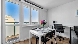 A modern apartment with a dining area, a workspace, and large windows offering a view of the city. - Mokotów Studio- 14th Floor, Balcony - by Rentujemy (Warszawa)