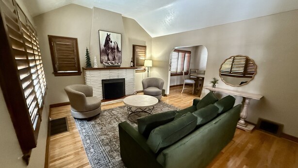 A living room with a fireplace, a green sofa, a round coffee table, and a fireplace mantel with a horse painting.