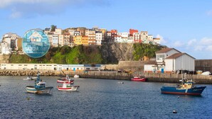 Un pueblo costero con edificios coloridos en una colina, barcos amarrados a lo largo del muelle y un cielo despejado.