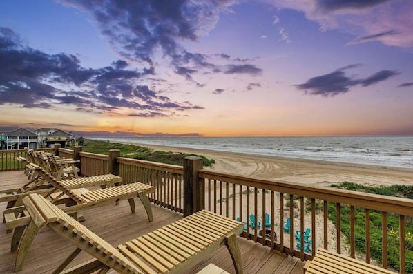 A wooden deck with lounge chairs overlooking a beach.