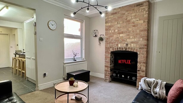 A living room with a fireplace, a sofa, a coffee table, and a TV displaying 'NETFLIX'. - 4-bed 3 Bath House in Leicester City (Leicester)