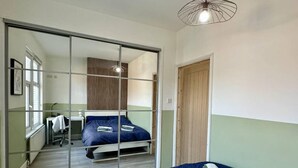 A bedroom with a large sliding door, a bed with blue bedding, a wooden door, and a desk with a chair. - 4-bed 3 Bath House in Leicester City (Leicester)