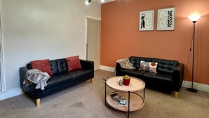 A living room with two black leather sofas, a round wooden coffee table, and a floor lamp. - 4-bed 3 Bath House in Leicester City (Leicester)