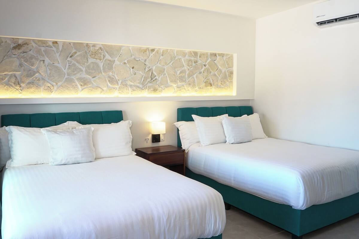 Ein Hotelzimmer mit zwei Betten, einem Kunstwerk aus Stein darüber und einem Nachttisch mit Lampe.