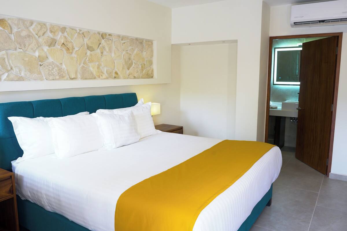 Ein Hotelzimmer mit einem großen Bett, einer Steinwand, einem Badezimmer mit Spiegel und einer Klimaanlage.