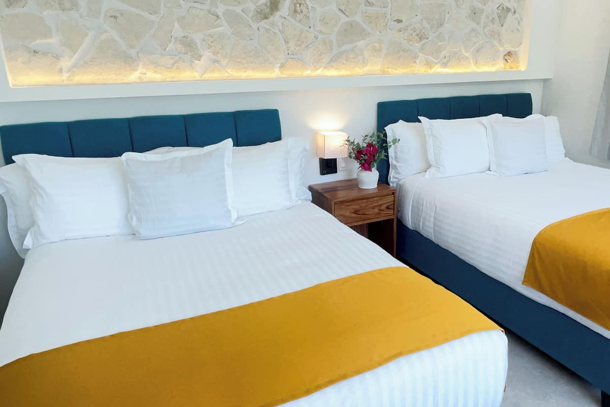 Ein Hotelzimmer mit zwei Betten, einer Steinwand, einem Nachttisch mit Lampe und einem Fenster mit Vorhängen.