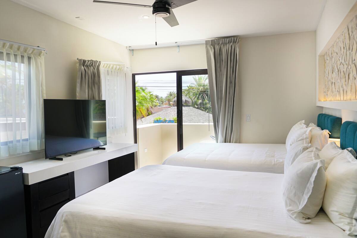 Ein Hotelzimmer mit Bett, Schreibtisch mit Fernseher und Balkon mit Vorhängen.