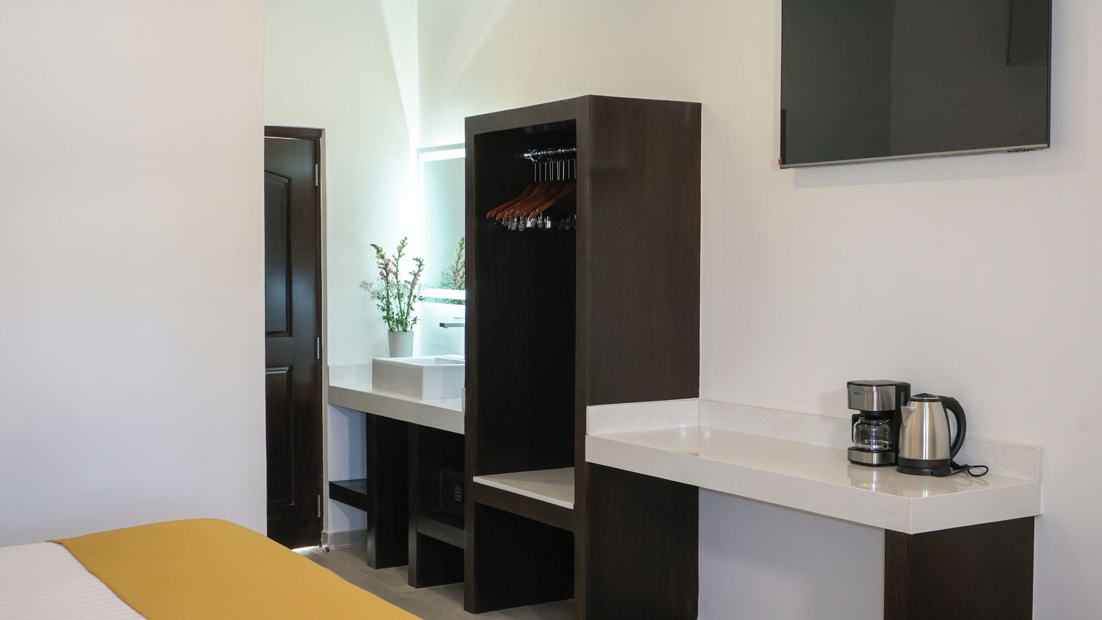 A modern bathroom with a white countertop, a dark wooden vanity, a mirror, and a coffee maker.