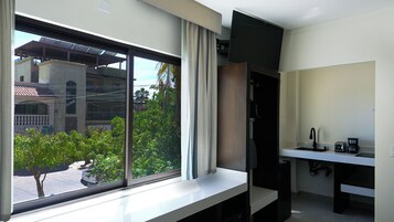 Quarto moderno com uma janela grande, uma escrivaninha embutida e uma pequena cozinha equipada.