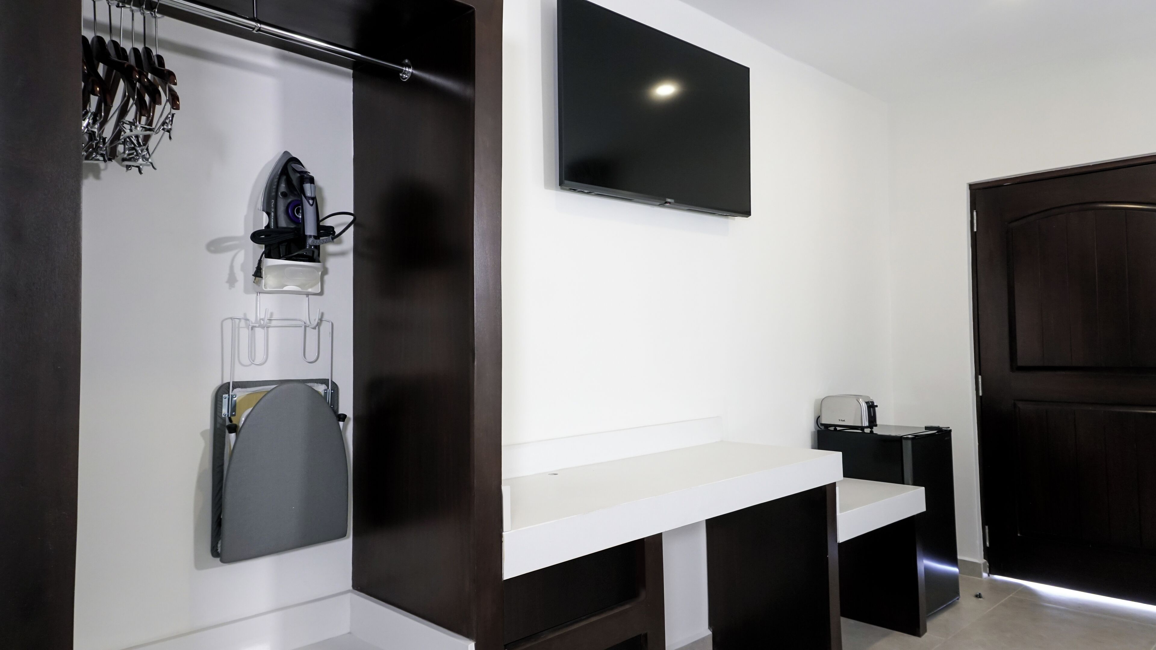 A modern bathroom with a white vanity, a mounted TV, and a dark wooden door.