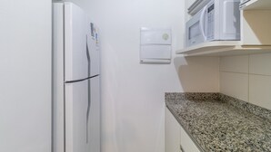 Une cuisine compacte avec un réfrigérateur blanc, un four à micro-ondes posé sur une étagère et un four encastré.