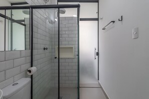 A modern bathroom with a glass-enclosed shower, white tiled walls, a toilet, and a towel rack.