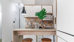 Une cuisine avec un comptoir-bar en bois, deux tabourets, une grande plante verte, un four à micro-ondes et un dosseret carrelé.