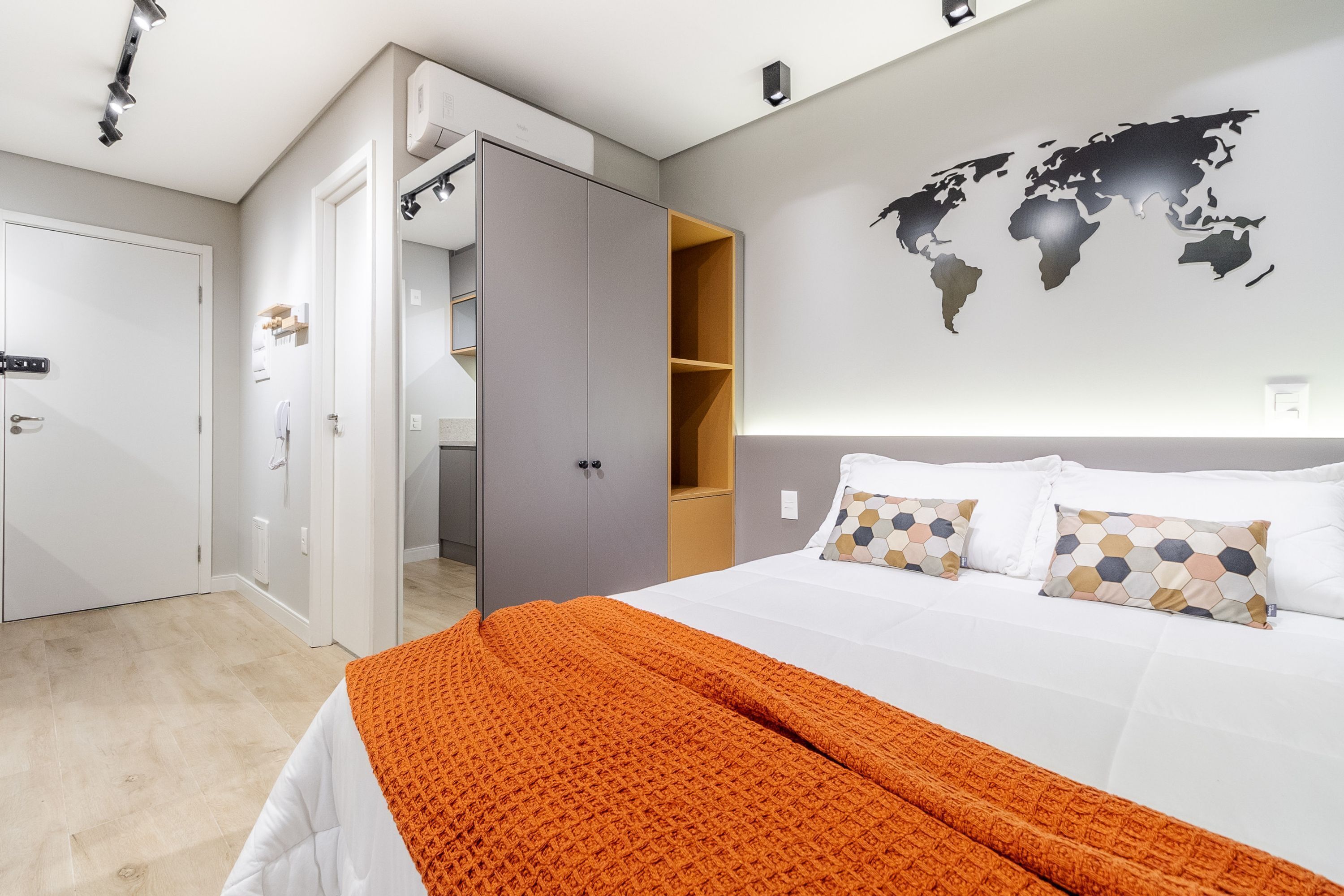 Una habitación de hotel moderna con una cama bien hecha, un mapa mundial en la pared y un armario con espejo.