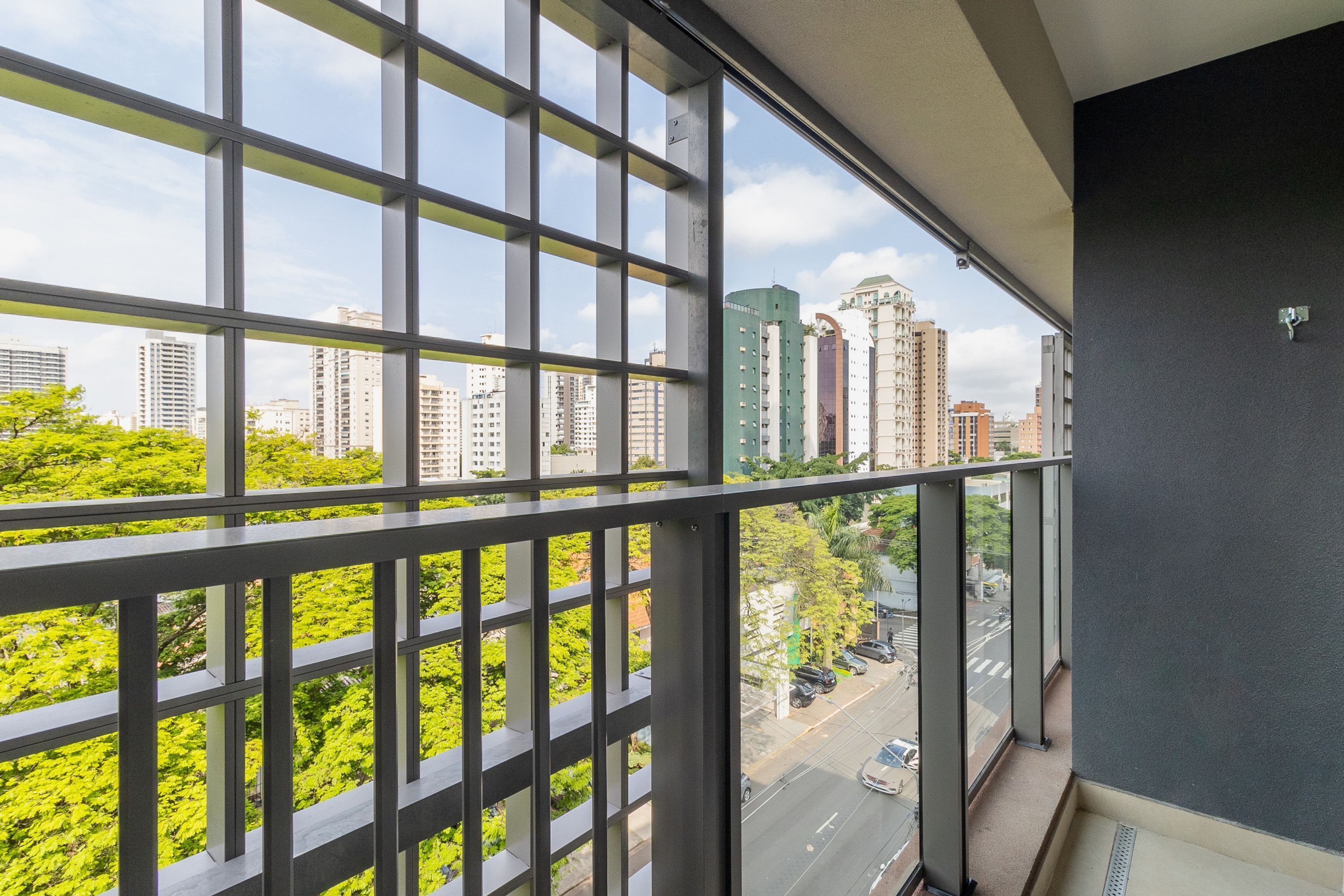 Uitzicht vanaf een balkon met een raster van ramen, uitkijkend op een stadsbeeld met hoge gebouwen en een groen park.