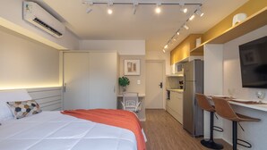 A modern hotel room with a bed, a desk with two chairs, a refrigerator, and a TV mounted on the wall. - Mingodoy in S o Paulo (São Paulo)