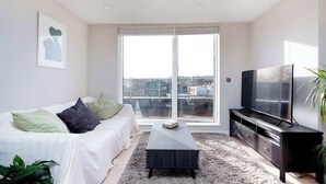 Un salon moderne avec un canapé, une table basse, un téléviseur et une grande fenêtre.