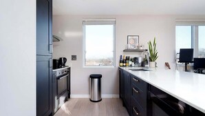 Une cuisine moderne avec des meubles de couleur sombre, une poubelle en acier inoxydable, une fenêtre et une vue sur l’extérieur.