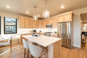 A modern kitchen with wooden cabinets, stainless steel appliances, and a large island with bar stools. - DVEV Condo-Year Round Activities-Communal Amenities-Free Ski Shuttle (Heber City)