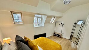 A bedroom with a bed, pillows, a bedside lamp, a window, and a wardrobe.