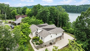 A two-story house with a stone foundation and a grey roof, surrounded by lush greenery and a lake. - 💦 Grande Villa – Lake Cumberland View • Game Room • Walk to Boat Ramp ➠ 389 (Somerset)