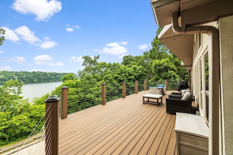 A wooden deck with outdoor furniture, overlooking a lake and forest.