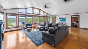 A spacious living room with a large gray sectional sofa, a blue rug, and a view of a lake through large windows. - 💦 Grande Villa – Lake Cumberland View • Game Room • Walk to Boat Ramp ➠ 389 (Somerset)