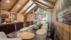 A rustic wooden interior with a dining area featuring a long table, woven placemats, and a central plant arrangement.