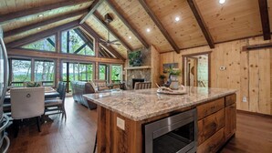 A spacious kitchen with a large island, wooden beams, and a stone fireplace.