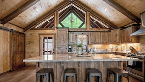 A rustic kitchen with a large island, wooden cabinets, and a vaulted ceiling.