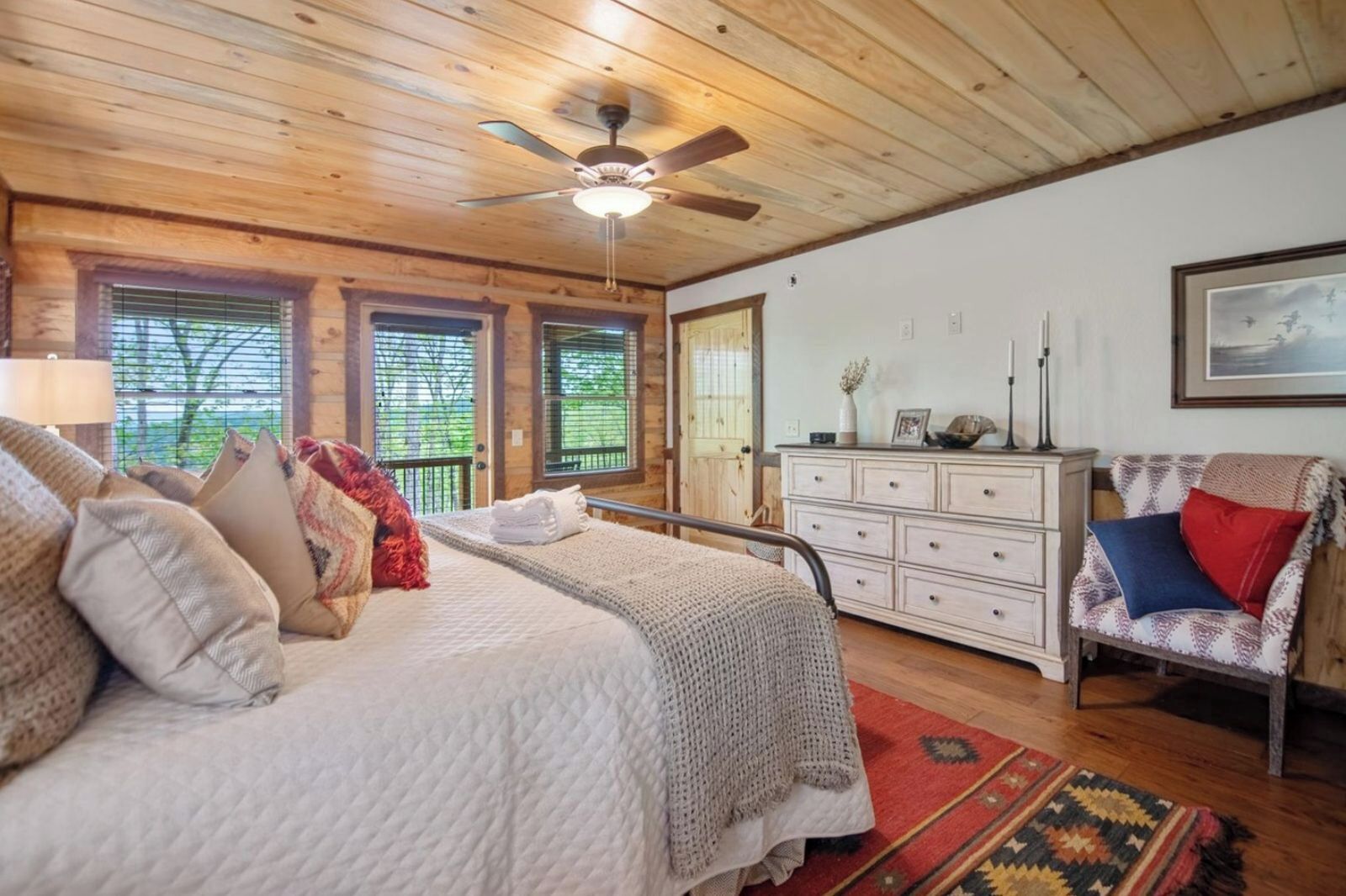 A cozy bedroom with a bed, dresser, chair, and a ceiling fan.