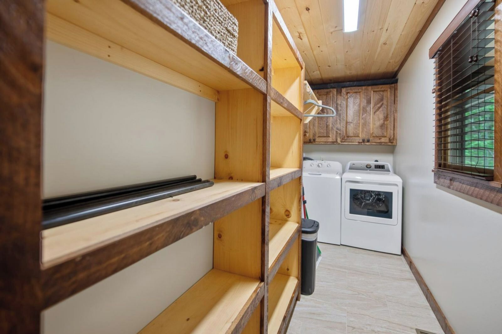 Une cuisine de taille réduite, dotée d’étagères en bois, d’un lave-linge et d’un sèche-linge.
