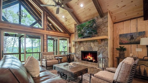 A cozy living room with a stone fireplace, leather sofas, and a large TV mounted on the wall.