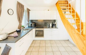 Una cocina con armarios blancos, estufa, lavabo y escalera de madera.