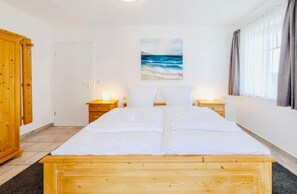Ein Schlafzimmer mit einem hölzernen Bett, zwei Nachttischen, einem Schrank und einem Meeresbild.