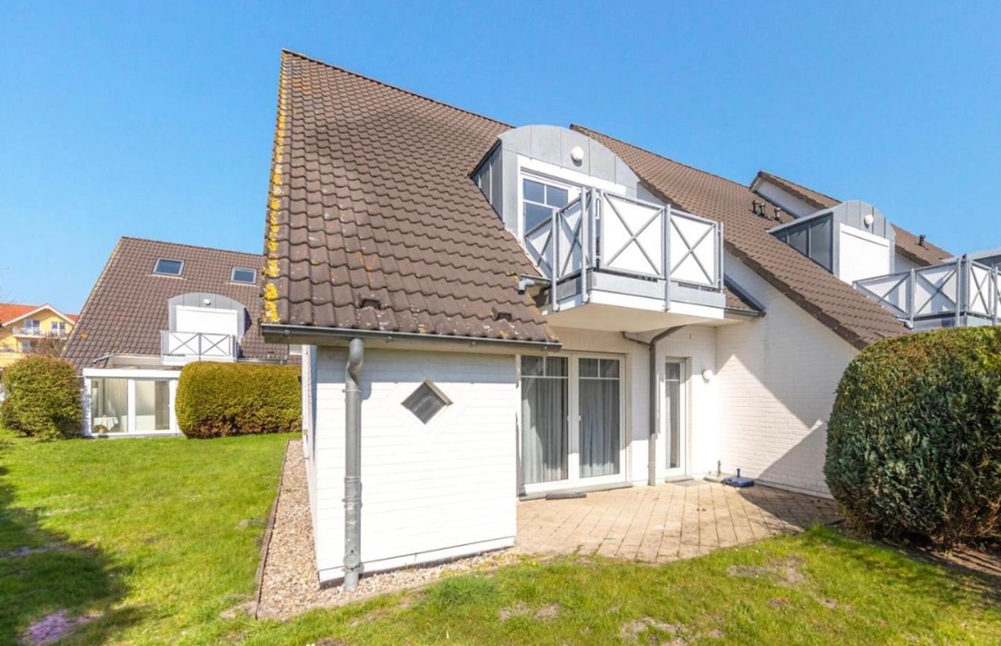 A two-story house with a sloped roof, a balcony, and a small garden area.
