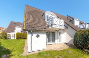 A two-story house with a sloped roof, a balcony, and a small garden area.