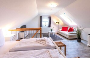 Un dormitorio acogedor en el ático con cama, una mesita pequeña, un sofá con cojines rojos y una planta en maceta.