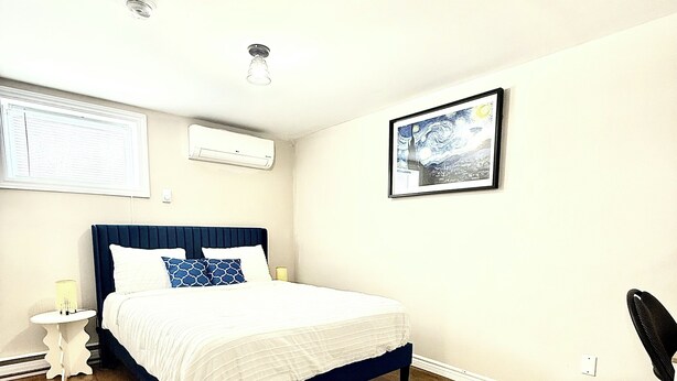 A bedroom with a bed, a nightstand, a chair, a patterned rug, and a painting on the wall.