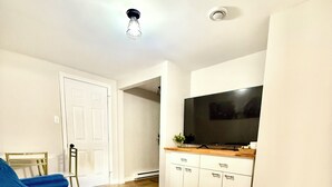 Un salon avec un canapé bleu, un téléviseur à écran plat posé sur un meuble en bois, des meubles blancs et un plancher en bois.