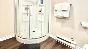 Une salle de bain d’angle avec une douche à parois de verre, des toilettes blanches et un porte-serviettes.