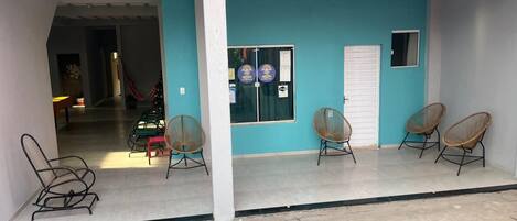 A building with a teal exterior, a covered porch with four wicker chairs, and a visible door with a sign.
