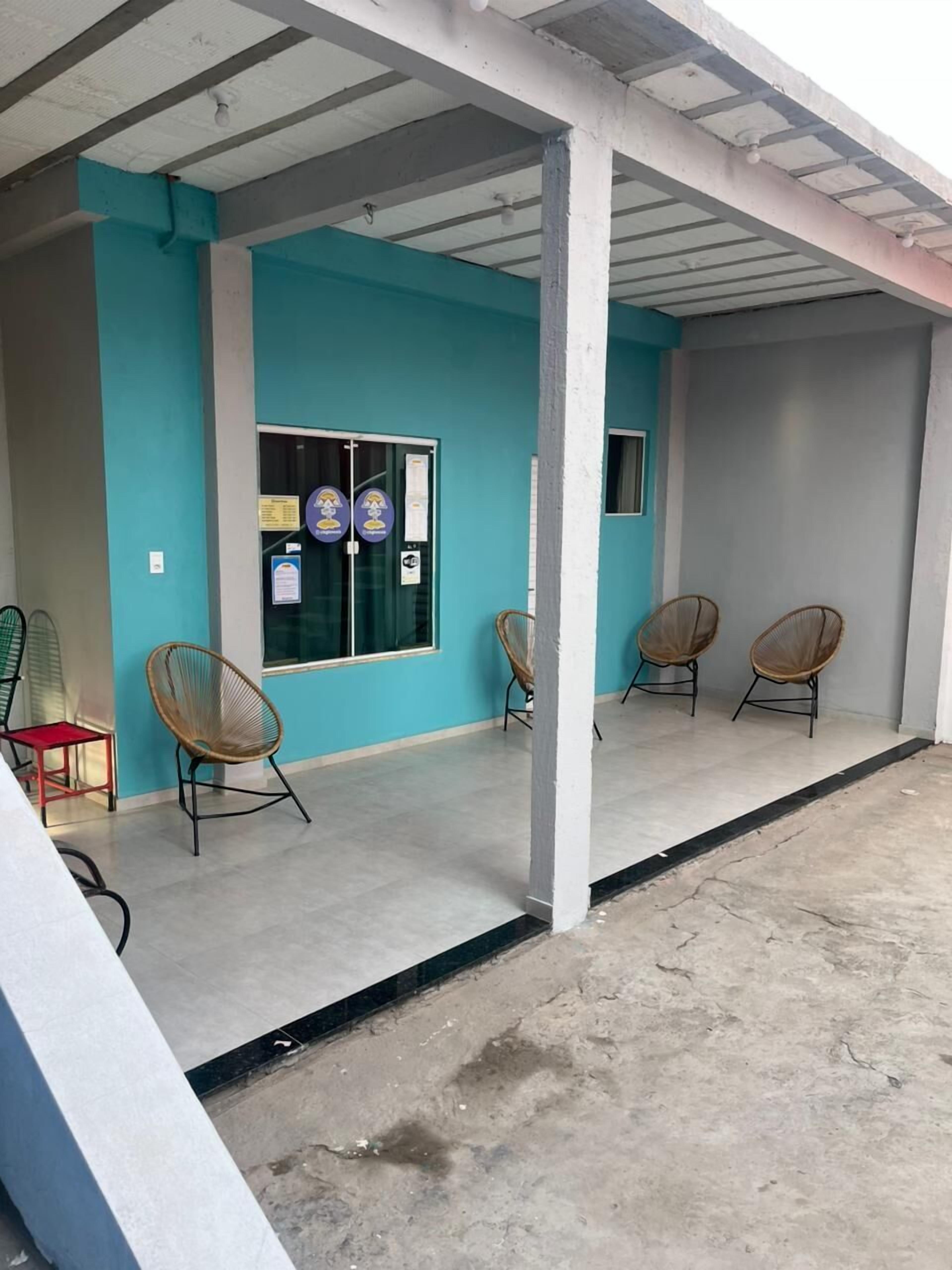 Un espacio al aire libre techado con una pared azul, un vidrio con pegatinas y tres sillas de mimbre.