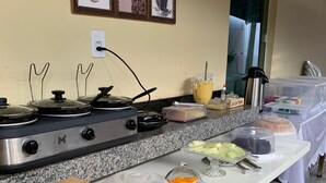A buffet setup with a stove, covered food containers, and a coffee-themed wall decoration. - Pousada BG Lençóis (Barreirinhas)