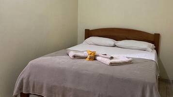 A neatly made bed with a checkered rug, a wooden headboard, and a plain wall.