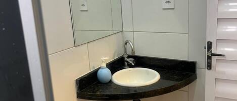 A small bathroom with a white sink, a mirror, and a black countertop.