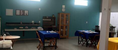 Un espace repas avec des tables et des chaises, un comptoir avec un évier et une horloge au mur.